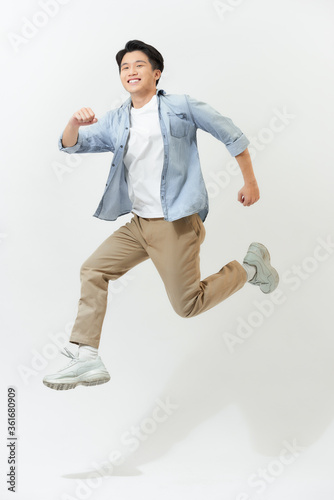 Energetic happy young Asian man in casual clothes jumping, studio shot isolated