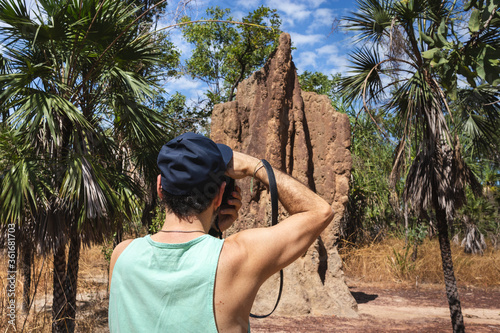 Tourist taking a picture of a big magnetic termite mound. Man pictured from behind wearing cap and t-shirt, holding camera. Summer time. Litchfield national park, Northern Territory NT, Australia photo