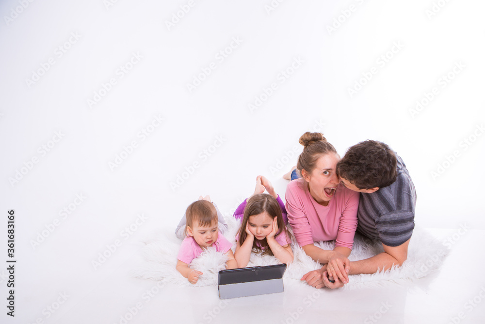 the kids are watching cartoons on the tablet. a man and a woman embrace. Family vacation, joint pastime. Parents with girls on the floor the kids are watching cartoons on the tablet. a man and a woman embrace. Family vacation, joint pastime. Parents with girls on the floor