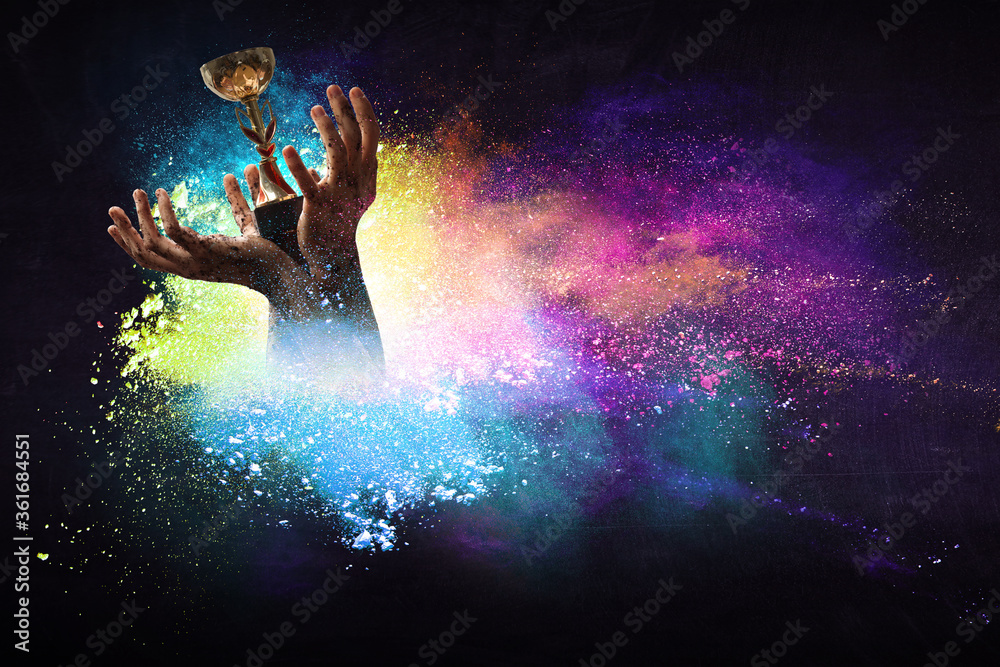 Hand holding up a gold trophy cup against dark background Hand holding up a gold trophy cup against dark background