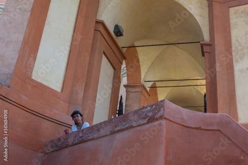 Woman in hat stadning on balcony surrounded by arches and plaster walls photo