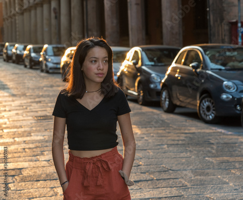 Young Asian teen in black blouse standing on stone street in front of building in black blouse