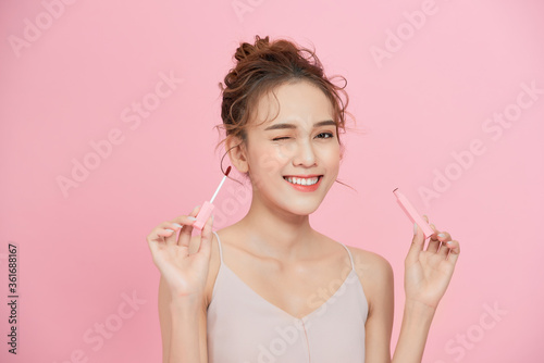 Young smiling Asian girl applying lipstick isolated over pink background.