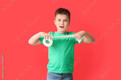 Funny little boy with toilet paper on color background