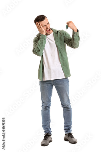 Angry man with alarm clock on white background. Concept of sleep deprivation