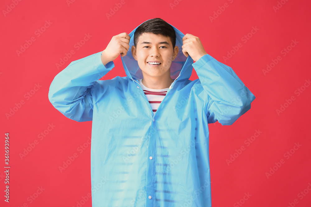 Young Asian man in raincoat on color background Young Asian man in raincoat on color background
