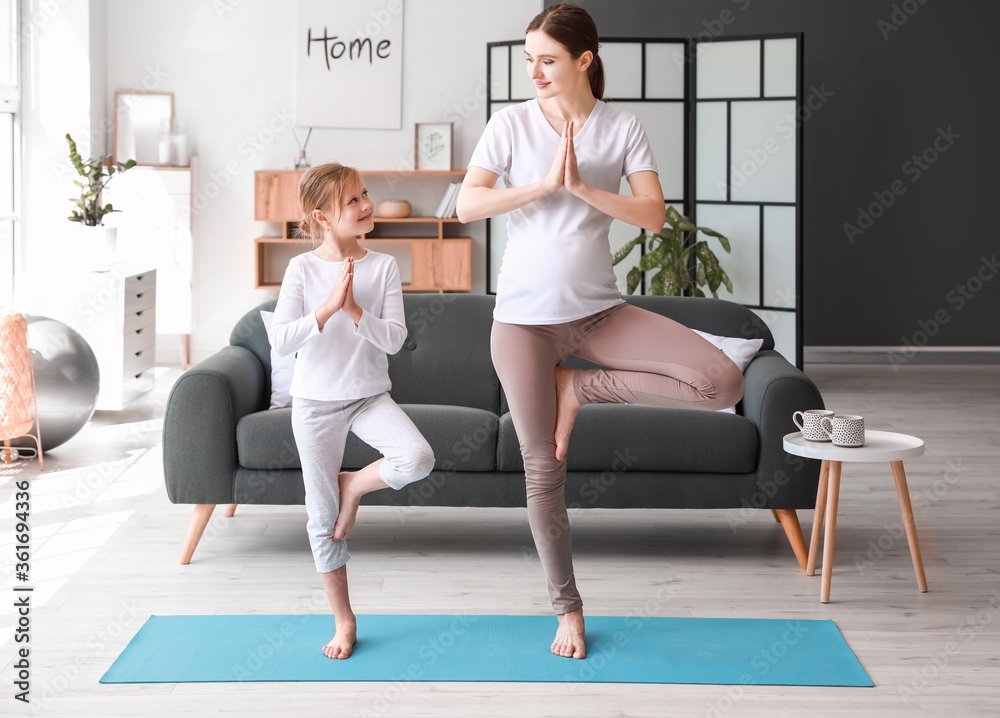 Obraz premium Young pregnant woman and her little daughter practicing yoga at home