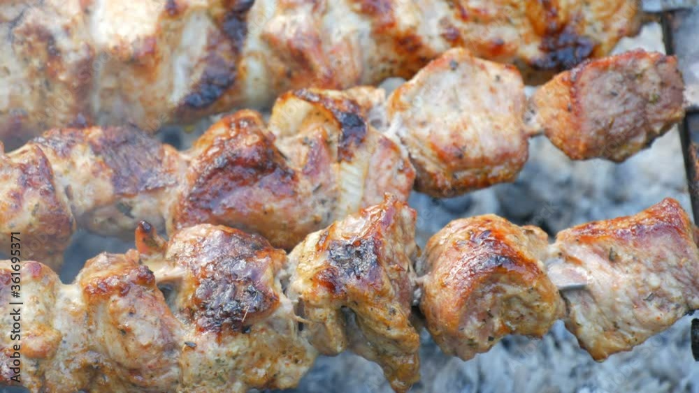Sliced pieces of meat on a skewer in the smoke. Pork skewers on the grill. Sliced meat with melting fat close up view in the garden of a country house Sliced pieces of meat on a skewer in the smoke. Pork skewers on the grill. Sliced meat with melting fat close up view in the garden of a country house