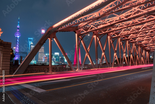 night view of Waibaidu Bridge, a historic landmark in Shanghai, with traffic inside and skyscrapers in then back. © Zimu
