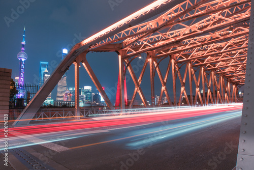 night view of Waibaidu Bridge, a historic landmark in Shanghai, with traffic inside and skyscrapers in then back. © Zimu