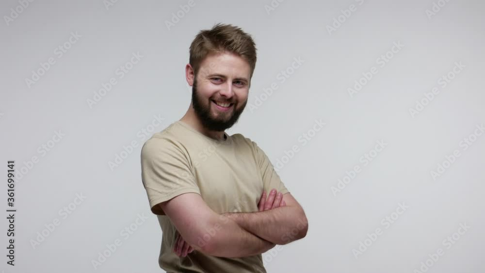 Cheerful handsome bearded guy turning crossed hands and looking at camera with toothy smile, feeling confident self-assertive, optimistic outlook. indoor studio shot isolated on gray background Cheerful handsome bearded guy turning crossed hands and looking at camera with toothy smile, feeling confident self-assertive, optimistic outlook. indoor studio shot isolated on gray background