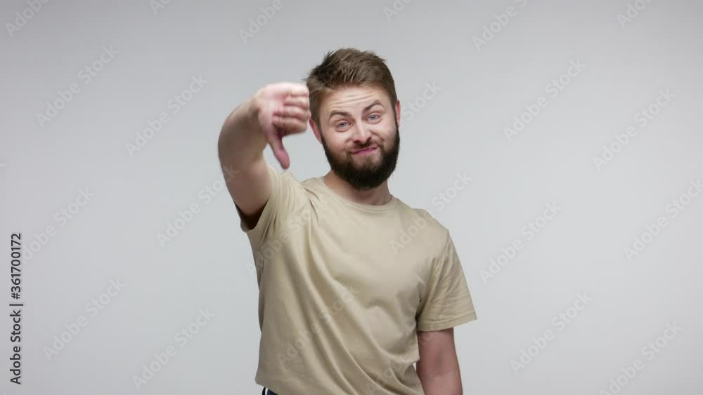 Displeased bearded guy looking at camera sarcastic dissatisfied, showing thumbs down, disapproval dislike gesture, negative critique and rejection. indoor studio shot isolated on gray background Displeased bearded guy looking at camera sarcastic dissatisfied, showing thumbs down, disapproval dislike gesture, negative critique and rejection. indoor studio shot isolated on gray background