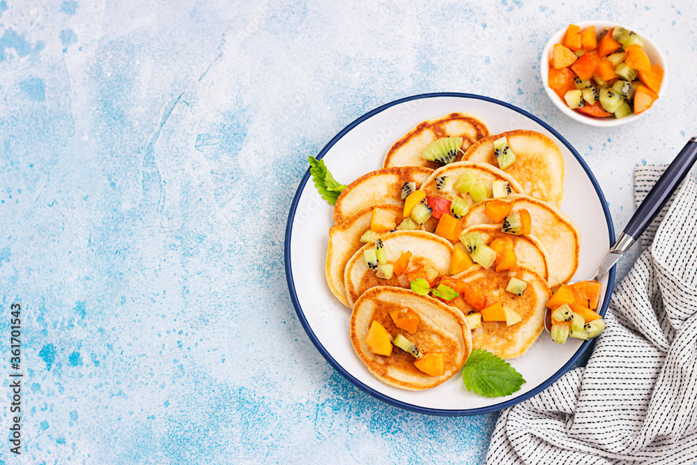 Classic pancakes garnish with apricot, kiwi and mint on ceramic plate, blue stone background. Top view. Classic pancakes garnish with apricot, kiwi and mint on ceramic plate, blue stone background. Top view.