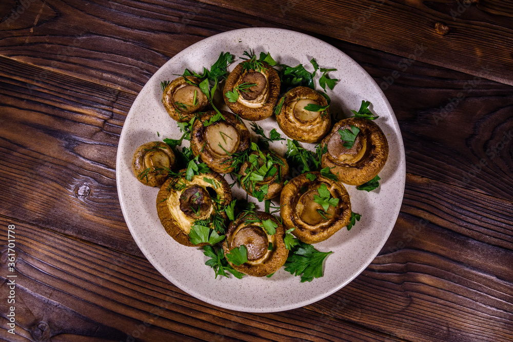 Plate with baked champignons, dill and parsley on a wooden table. Top view Plate with baked champignons, dill and parsley on a wooden table. Top view