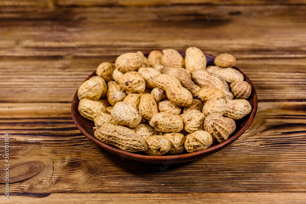Ceramic plate with heap of unpeeled peanuts on wooden table Ceramic plate with heap of unpeeled peanuts on wooden table