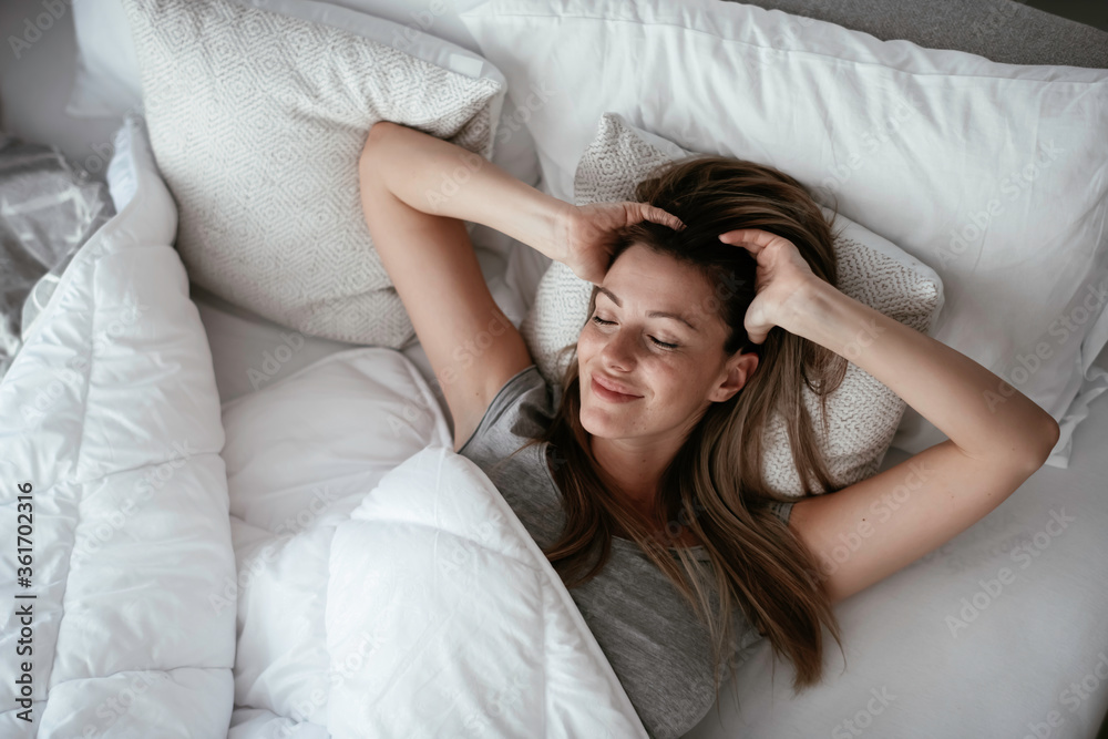 Fototapeta premium Woman stretching in bed after wake up. Beautiful girl enjoying morning light.