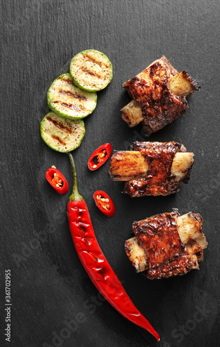 Tasty beef short ribs with vegetables on dark background