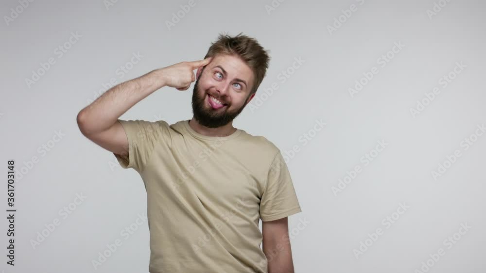 I am idiot! Funny bearded man gesturing finger against temple doing stupid gesture, looking at camera with dumb brainless silly expression, cuckoo out of mind. studio shot isolated on gray background I am idiot! Funny bearded man gesturing finger against temple doing stupid gesture, looking at camera with dumb brainless silly expression, cuckoo out of mind. studio shot isolated on gray background