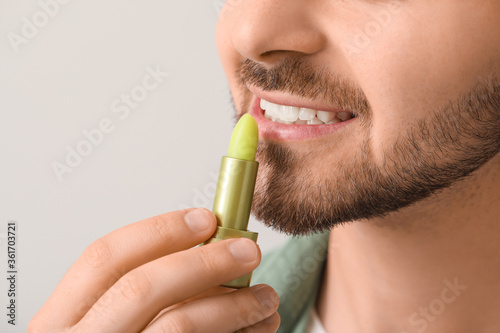 Handsome young man with lip balm on light background, closeup