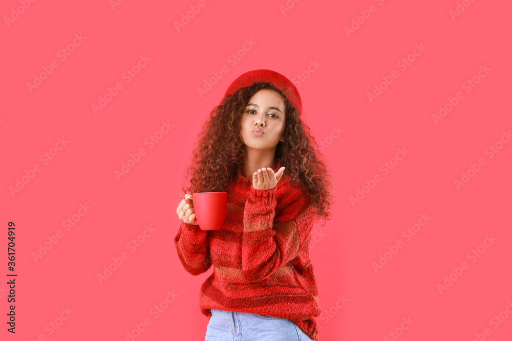 Beautiful young African-American woman with hot tea blowing kiss on color background Beautiful young African-American woman with hot tea blowing kiss on color background