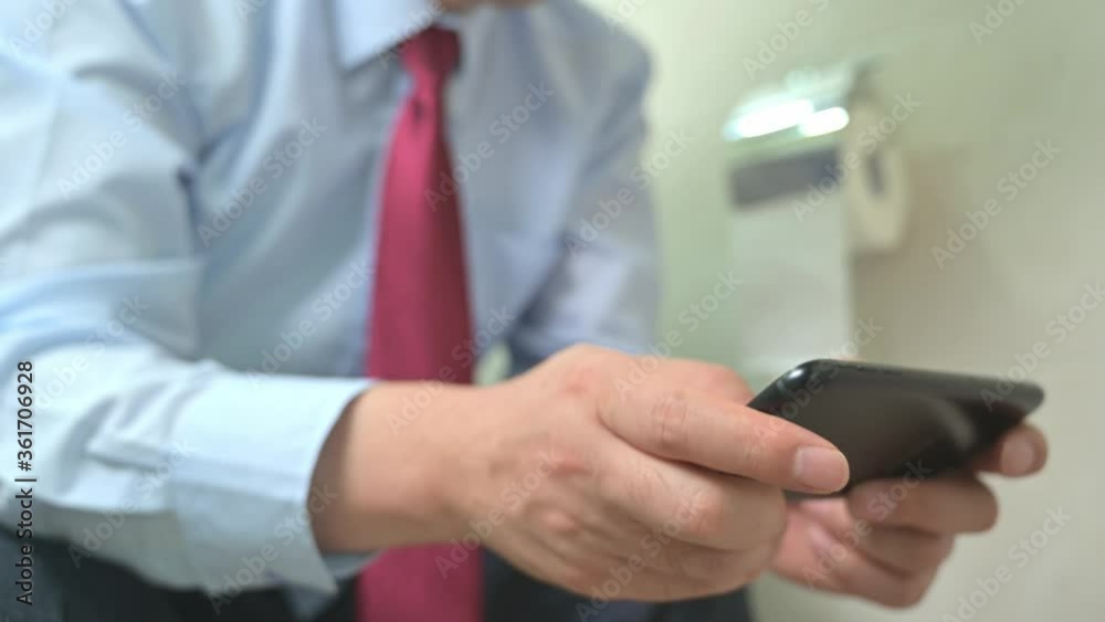 Businessman sitting on the toilet in the bathroom and using a smartphone. Businessman sitting on the toilet in the bathroom and using a smartphone.