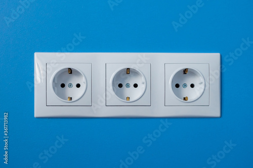 Group of empty, unplugged white electrical european outlet, socket located on blue wall - close up front view. Equipment, design, electricity, energy, technology concept