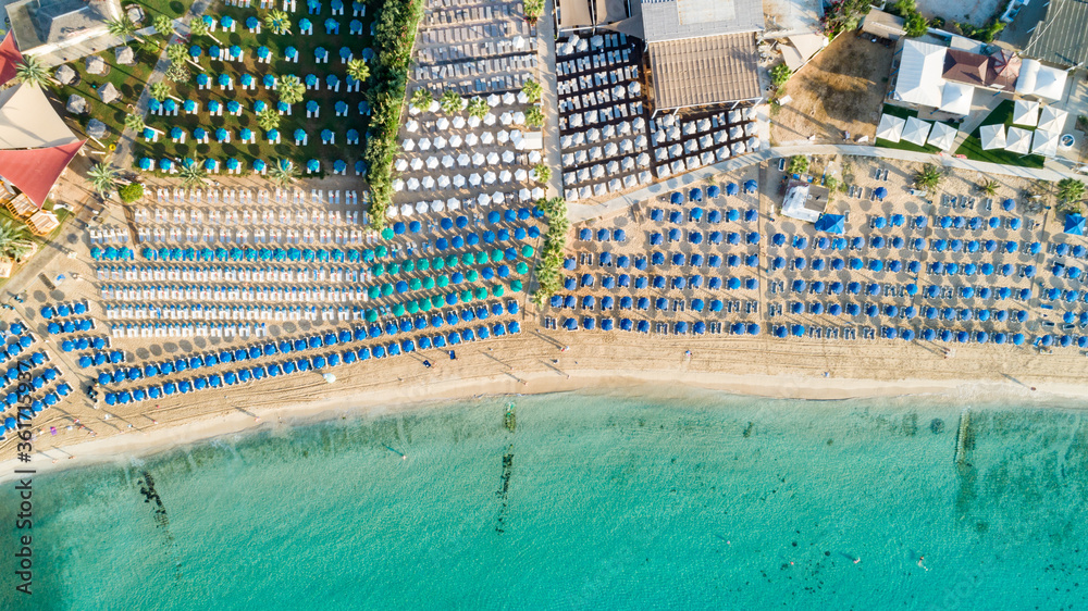 Aerial above bird's eye view of Pantachou - Limanaki organised beach (Kaliva), Ayia Napa, Famagusta, Cyprus. Blue aligned umbrellas, golden sand, parasols, sunbathing sea beds clean turquoise water