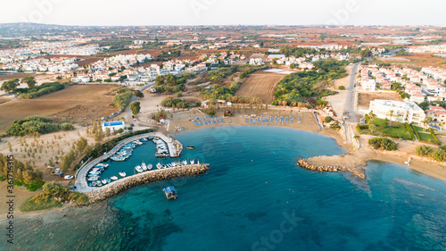 Aerial bird's eye view of coastline sunset, landmark white washed chapel Agia Triada beach, Protaras, Famagusta, Cyprus from above. Tourist attraction Ayia Trias bay church, sand, port at sunrise.