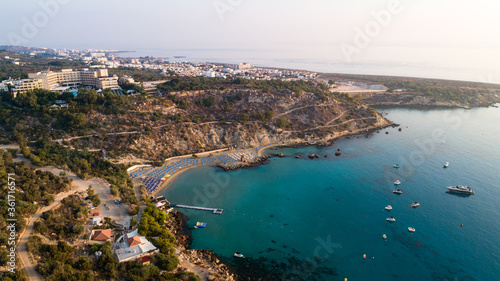 Aerial bird's eye view of Konnos beach, Cavo Greco Protaras, Paralimni, Famagusta, Cyprus. Famous tourist attraction golden sandy bay with boats, yachts in the sea, sunbeds, water sports, from above.