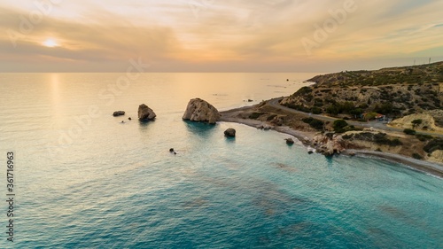 Aerial Bird's eye view of Petra tou Romiou, aka Aphrodite's rock a famous tourist travel destination landmark in Paphos, Cyprus. The sea bay of goddess Afroditi birthplace at sunset from above. photo