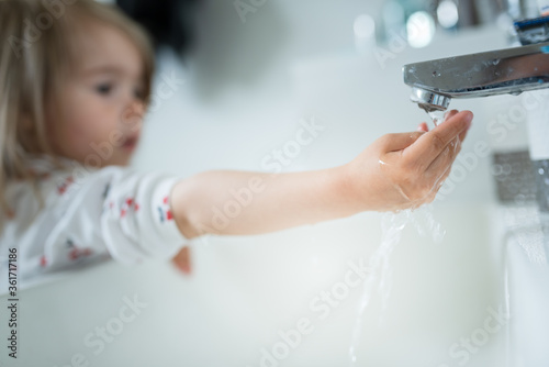 Cute little girl 2-3 years old washing hands with soap and water in bright bathroom.