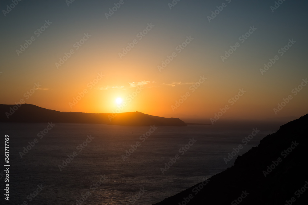 Sunset over the sea and the south end of the island of Santorini, Greece. View from Fira, the capital