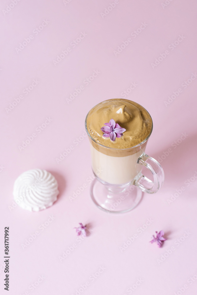 Beautiful dalgon coffee drink. Coffee mug in clear glass with foam and lilac flower on a lilac background. Sweetness to the drink-marshmallow Beautiful dalgon coffee drink. Coffee mug in clear glass with foam and lilac flower on a lilac background. Sweetness to the drink-marshmallow