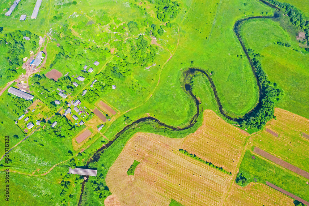 Obraz premium Top aerial view of the natural rural landscape valley of a meandering river among green fields and forests.