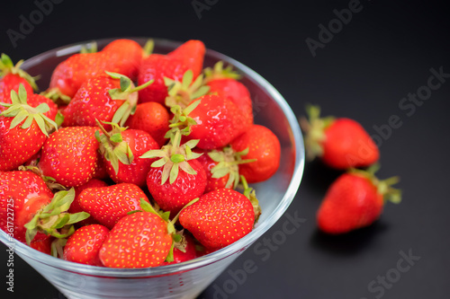Fresh organic strawberries in  glass bowl  on  black table.