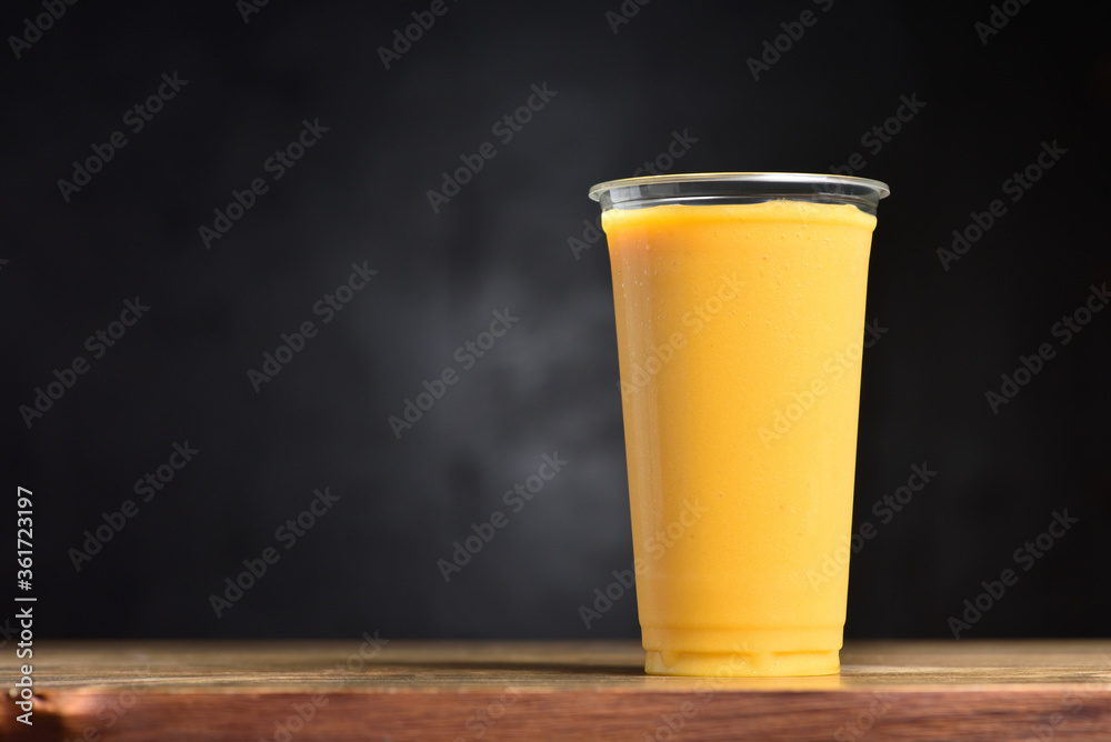 Fruit smoothie in a plastic glass. Summer drink of mango, banana, ice and juice on a black background with copy space Fruit smoothie in a plastic glass. Summer drink of mango, banana, ice and juice on a black background with copy space
