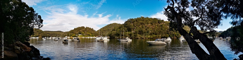 Beautiful morning panoramic view of Creek with boats and reflections of blue sky, light clouds, mountains and trees. Berowra Waters, Berowra Valley National Park, New South Wales, Australia Beautiful morning panoramic view of Creek with boats and reflections of blue sky, light clouds, mountains and trees. Berowra Waters, Berowra Valley National Park, New South Wales, Australia