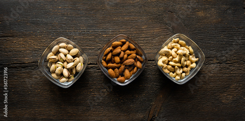 Almond, pistachio and cashew in a small plates which standing on a vintage wooden table. Nuts is a healthy vegetarian protein and nutritious food.