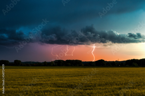 Thunderstorm atmosphere with lightning over wheat fields with cloudy sky and view of Inningen near Augsburg