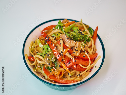 Udon noodles with meat in a plate on a white surface. With vegetables greens