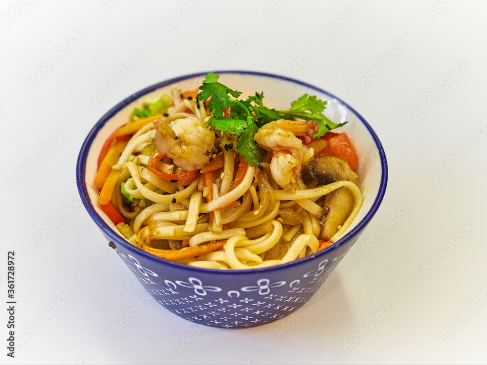 Udon noodles with seafood in a plate on a white surface. With vegetables greens