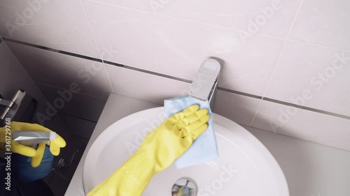 The girl washes a silver faucet. Apply detergent from a spray.