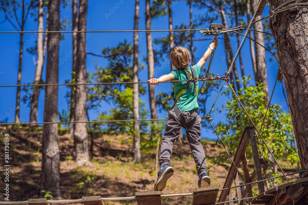 Portrait of cute little boy walk on a rope bridge in an adventure rope park Portrait of cute little boy walk on a rope bridge in an adventure rope park
