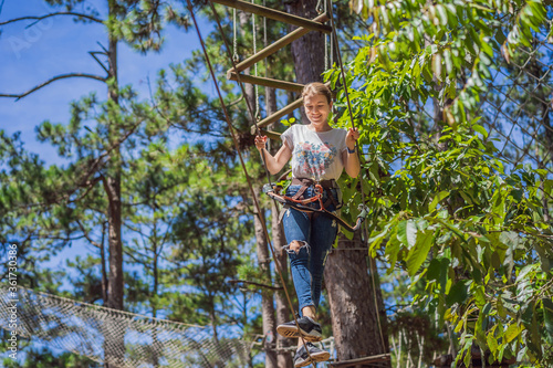 Young attractive woman in adventure rope park in safety equipment