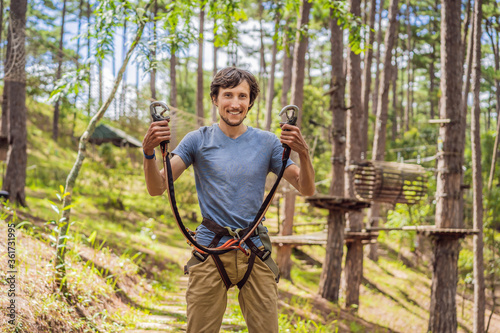 Young attractive man in adventure rope park in safety equipment