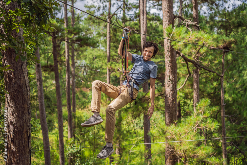 Young attractive man in adventure rope park in safety equipment