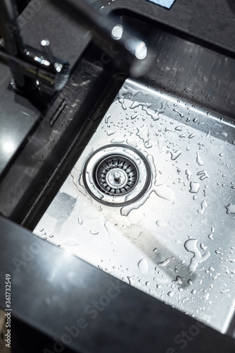 Modern water tap and sink, made of stainless steel. Drainage. Some water drops at the bottom. photo