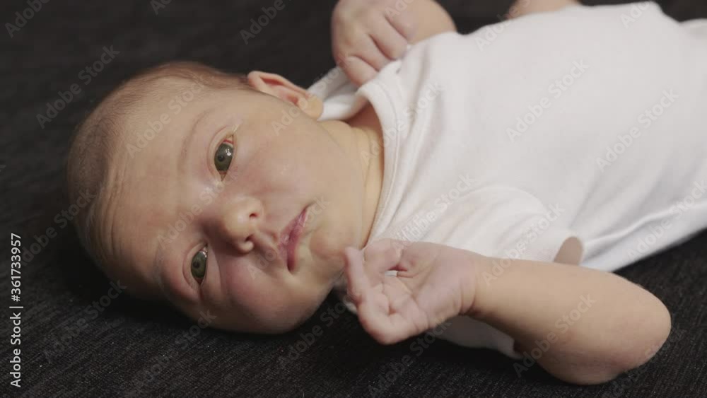 Portrait of a newborn baby lies on a black bedspread and opens his mouth. First moments of life. Close-up of newborn baby face portrait. Portrait of a newborn baby lies on a black bedspread and opens his mouth. First moments of life. Close-up of newborn baby face portrait.