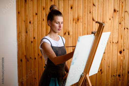 young female artist paints on canvas at the easel