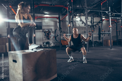 Beautiful young sporty couple training, workout in gym together. Caucasian man training with female trainer. Concept of sport, activity, healthy lifestyle, strength and power. Working out with barbell